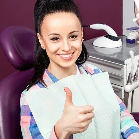 A young woman holding up a thumbs up while sitting in a dental exam chair