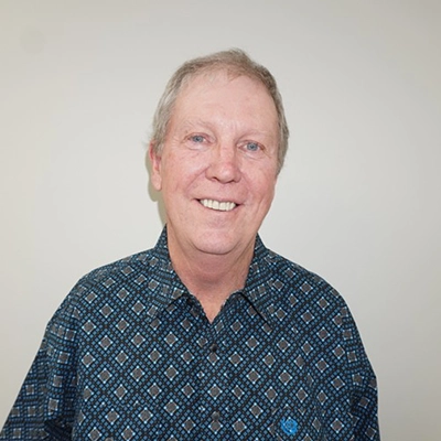 John Burns smiling in front of a white wall.