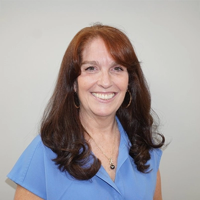 Sally Pope- Burns smiling in front of a white wall.